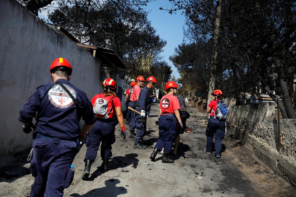 Members of a rescue team search an area following a wildfire at the village of Mati, near Athens, Greece.