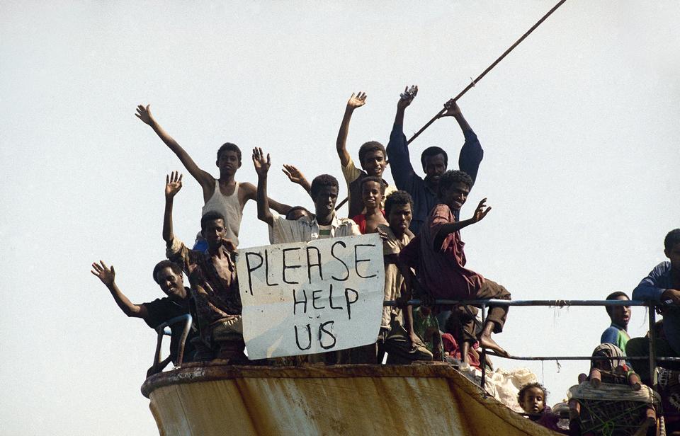 Somali refugees wave happily behind a sign calling for help as their ship Samaa-1 enters Yemen's Aden harbor on Wednesday, November 18, 1992 after more than a week at sea.