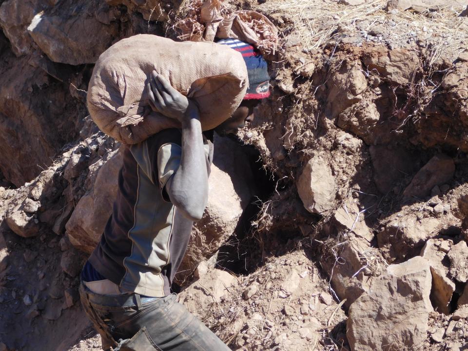A miner carries a sack of gold ore from a pit at Gaika Mine for panning at a water point.