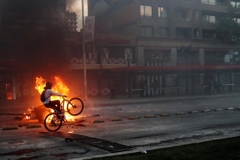 A demonstrator rides a bicycle past an improvised bonfire during a protest against the increase in subway ticket prices in Santiago, Chile, October 19, 2019.
