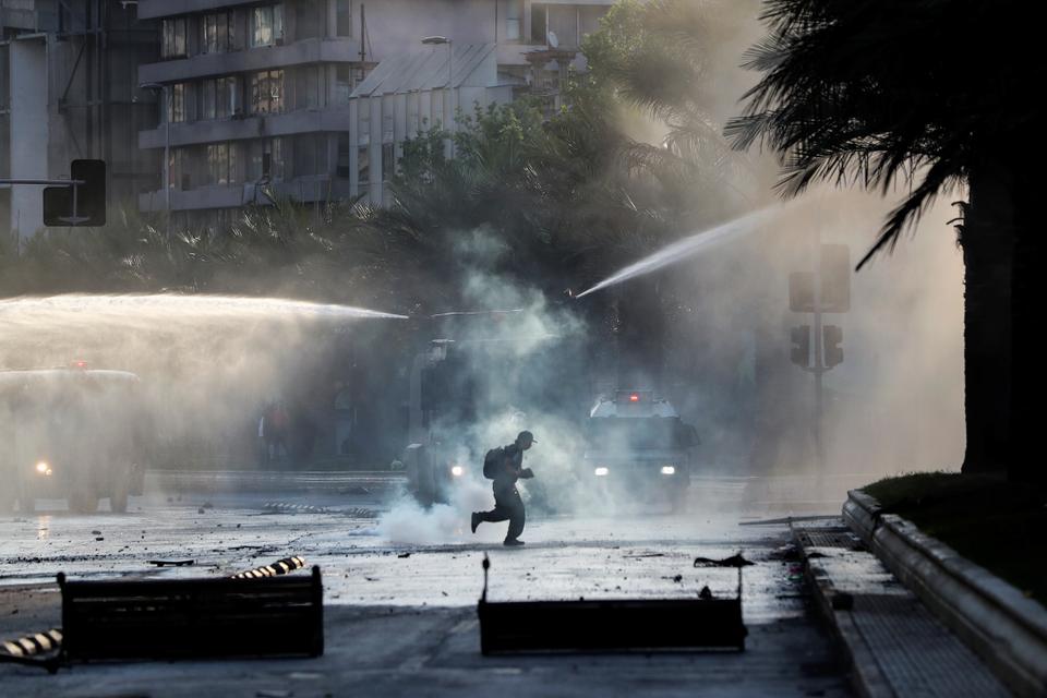 A demonstrator runs past police water cannons and tear gas deployed during a protest against the increase in subway ticket prices in Santiago, Chile, October 19, 2019.