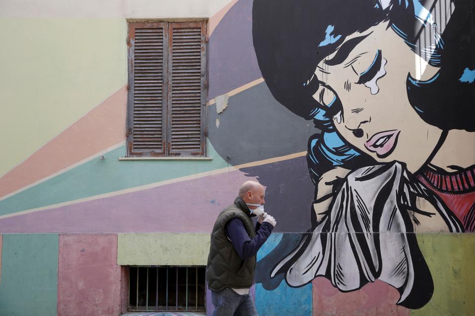A man adjusts his face mask as he walks past a mural of a crying woman in Rome's Trullo neighborhood, Monday, March 16, 2020.