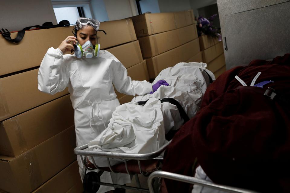 Alisha Narvaez, 36, the manager at International Funeral & Cremation Services, a funeral home in Harlem, stands in front of a row of deceased people stored inside cardboard boxes that are assigned to be cremated, as she takes a phone call, during the coronavirus disease (COVID-19) outbreak, in Manhattan, New York City, New York, U.S., April 9, 2020.