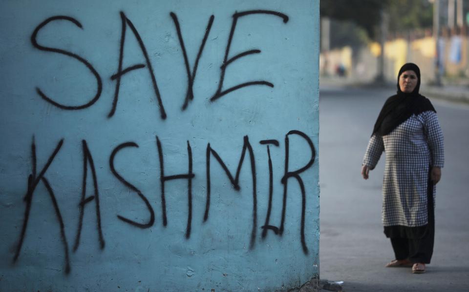 A Kashmiri woman stands next to a graffiti written on a wall during restrictions, following scrapping of the special constitutional status for Kashmir by the Indian government, in Srinagar, Indian-administered Kashmir, September 15, 2019.