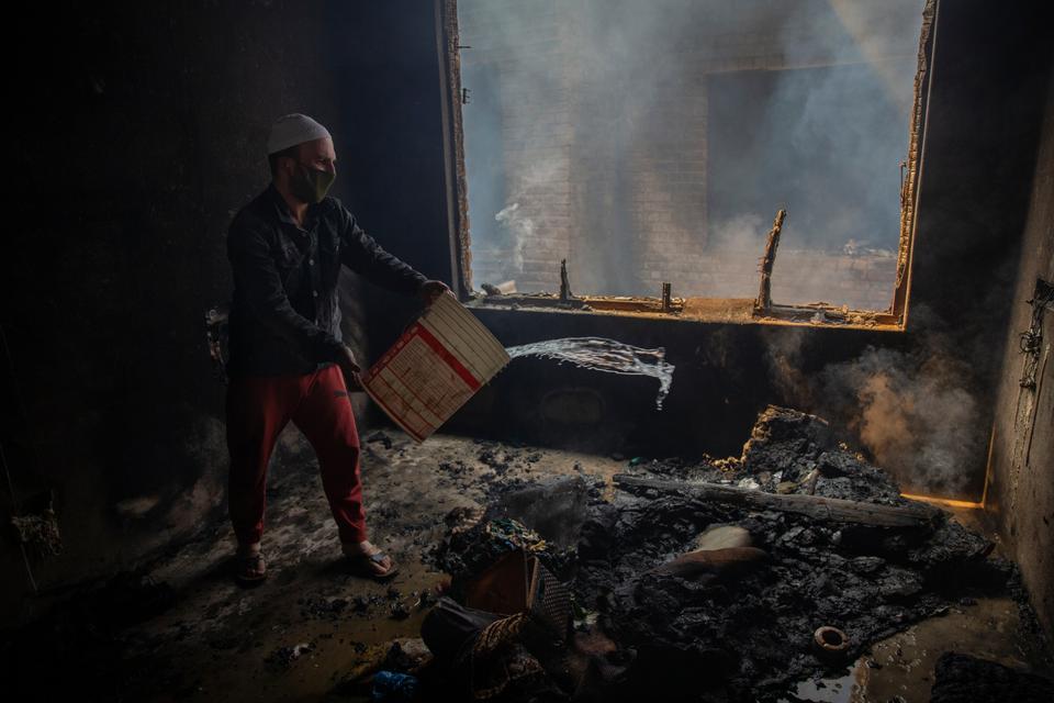 A Kashmiri man douses a house fire that started as a result of a gun-battle in Srinagar, Indian-controlled Kashmir, Tuesday, May 19, 2020.