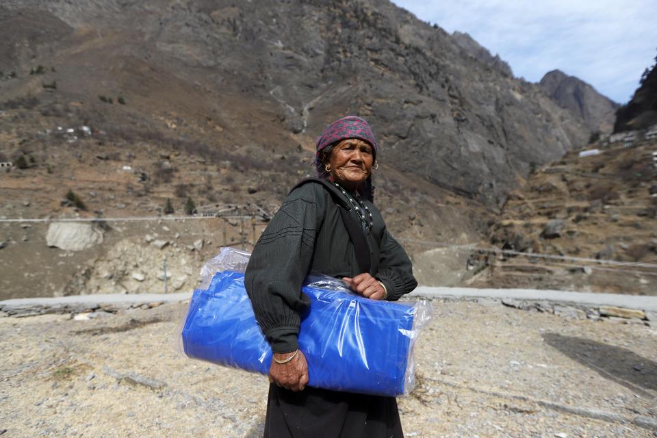 An old woman of Raini village carries the tarpaulin sheet provided by Sikh charity organisation Khalsa Aid.